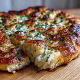 Freshly baked The Best Easy Garlic Naan Bread piled high with minced garlic and herbs on a wooden board.