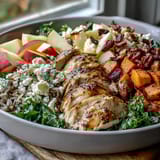 Close-up of a Harvest Bowl drizzled with tangy balsamic dressing, showing glistening greens, tender grains, and creamy crumbles.