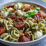 Colorful pasta salad with basil pesto, juicy cherry tomatoes, and creamy mozzarella, perfect for warm-weather picnics or easy dinners.
