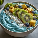 Creamy blue spirulina smoothie bowl breakfast topped with colorful fresh fruit.
