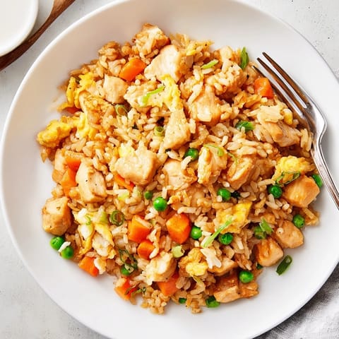 A large skillet holds steaming hot jasmine rice mixed with tender chicken, vibrant green peas, and sliced scallions, ready to serve as Chicken Fried Rice.
