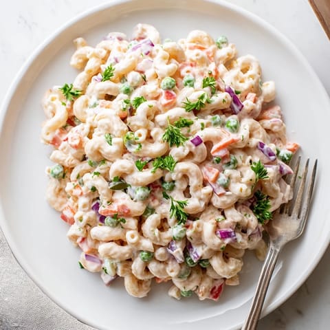 Tender elbow macaroni tossed with carrots, peas, and a tangy mayonnaise dressing in a serving bowl.