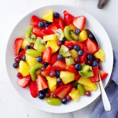 Fruit Salad glistens in a glass bowl, featuring sliced strawberries, kiwi, and juicy pineapple.