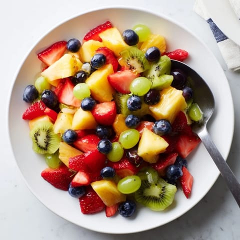 A close-up of Fruit Salad showcases halved grapes and blueberries tossed in citrus syrup.