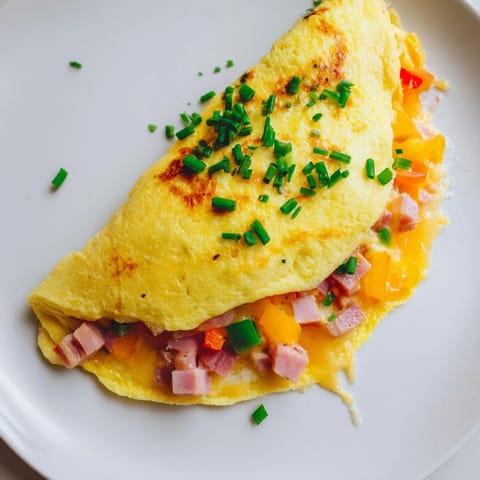 Golden-brown omelet with cheese revealing melted Gruyère and fresh chives, served alongside crusty bread and butter.