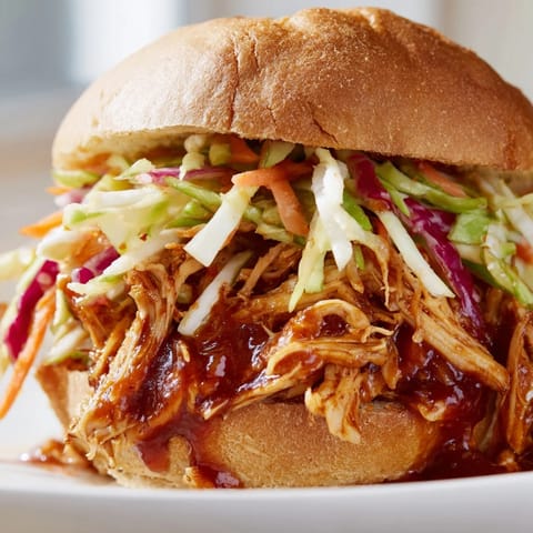 The golden-brown brioche bun cradles tender pulled barbecue chicken, generously topped with bright, crunchy slaw for a perfect bite.  