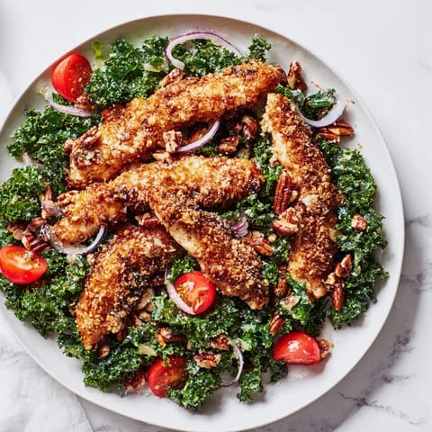 Fresh kale salad topped with pan-fried chicken cutlets, red onions, and pecans, drizzled with a sweet mustard vinaigrette.