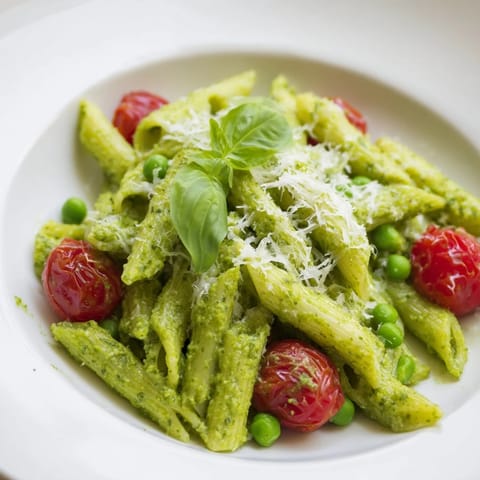 Bright Green Pesto Pasta Salad with halved cherry tomatoes, sweet peas, and grated Parmesan served in a white bowl.