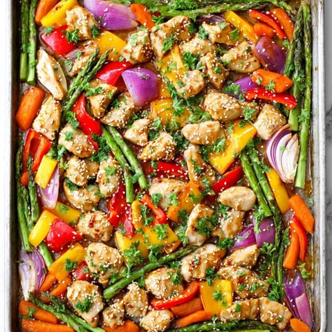 A close-up view showcases tender chicken bites and roasted spring vegetables, like sugar snap peas and baby carrots, coated in a savory-sweet honey garlic glaze.