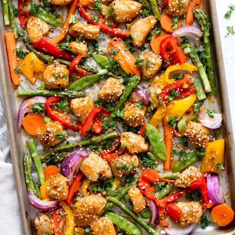 Golden, caramelized pieces of Sheet Pan Honey Garlic Chicken mingle with vibrant red bell peppers and crisp asparagus spears on a parchment-lined pan, glistening with a glossy sauce.