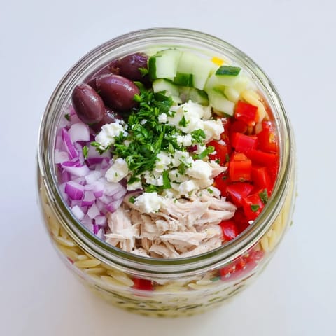 Layered Greek Pasta Chicken Salad Jar with orzo, juicy chicken, tomatoes, cucumbers, and feta cheese, ready for lunch.