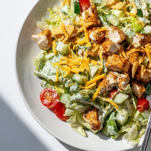 A generous drizzle of spicy jalapeño ranch coats chopped chicken and fresh vegetables in this vibrant salad, topped with shredded cheddar and crispy tortilla strips for irresistible texture and flavor.