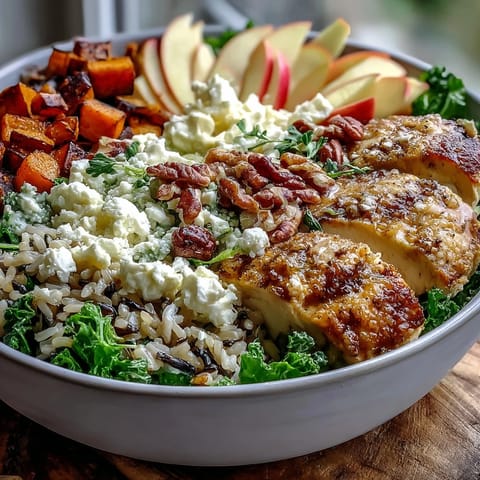 Colorful Harvest Bowl with roasted sweet potatoes and sliced chicken over kale and wild rice, topped with apple, almonds, and goat cheese.
