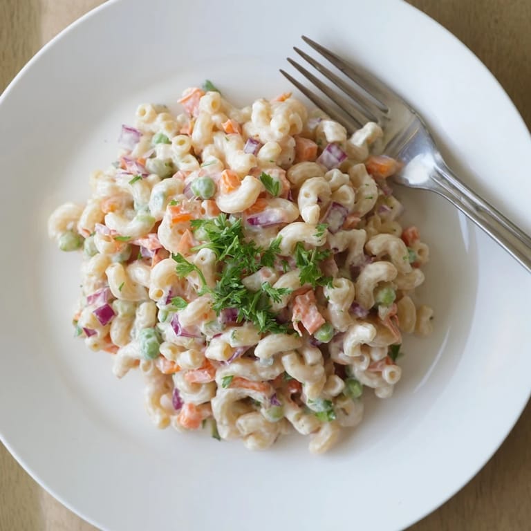 A bowl of homemade macaroni salad garnished with fresh parsley, ready for a summer picnic.