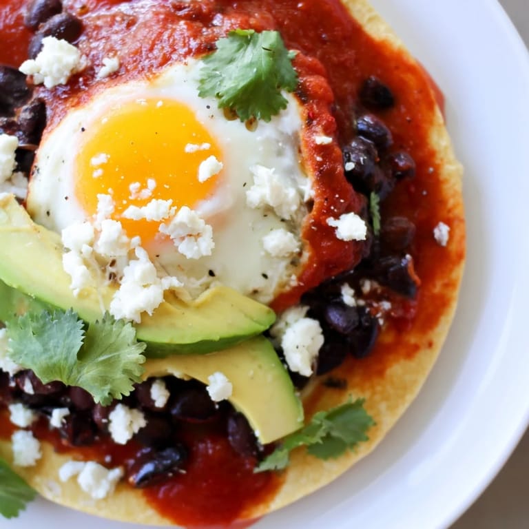 Hearty vegetarian Huevos Rancheros breakfast with creamy avocado slices, crumbled queso fresco, and warm black beans on the plate.