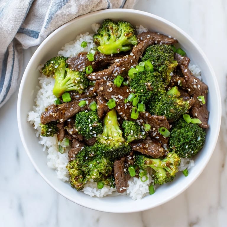 Colorful beef and broccoli stir-fry garnished with sesame seeds and fresh green onions over white rice.