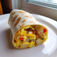 Hearty breakfast burrito with fluffy scrambled eggs, crispy potatoes, and melted cheddar cheese wrapped in a warm flour tortilla.