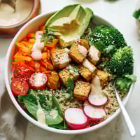 A vibrant Buddha Bowl with baked tofu, avocado slices, quinoa, and colorful vegetables drizzled with creamy tahini dressing.