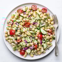 A vibrant bowl of Lemon Herb Chickpea Pasta Salad with diced cucumber, halved cherry tomatoes, and fresh dill in a zesty lemon dressing.