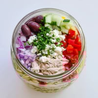 Layered Greek Pasta Chicken Salad Jar with orzo, juicy chicken, tomatoes, cucumbers, and feta cheese, ready for lunch.