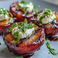 Freshly grilled plums with grill marks topped with creamy goat cheese and a drizzle of tangy balsamic glaze on a serving platter.