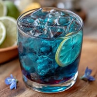 Butterfly Pea Flower Color-Change Lemonade with vibrant blue hue and fresh lemon slices, transforming into a stunning purple when citrus is added.